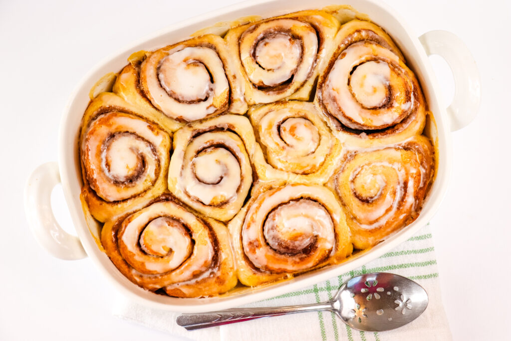 viral tiktok cinnamon rolls in large white baking dish with serving spoon beside it