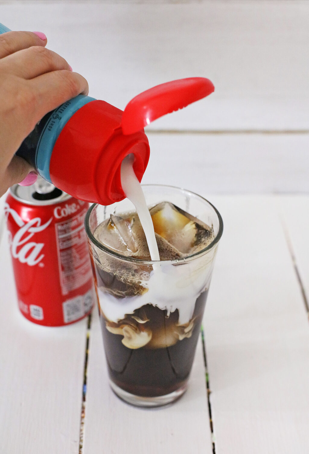 hand pouring creamer into glass with soda