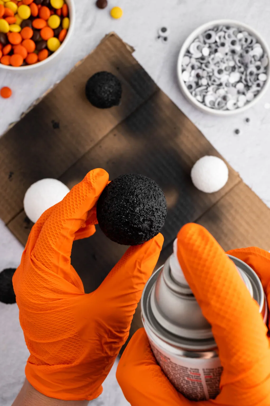 hand wearing orange gloves to spray paint styrofoam balls with black spray paint