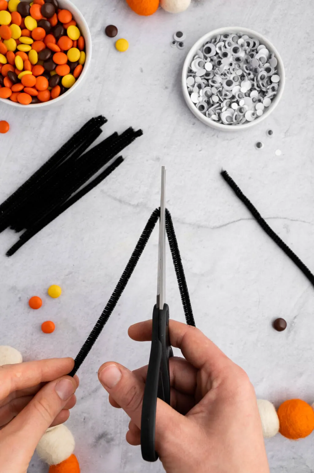 hands using scissors to cute black pipe cleaners in half
