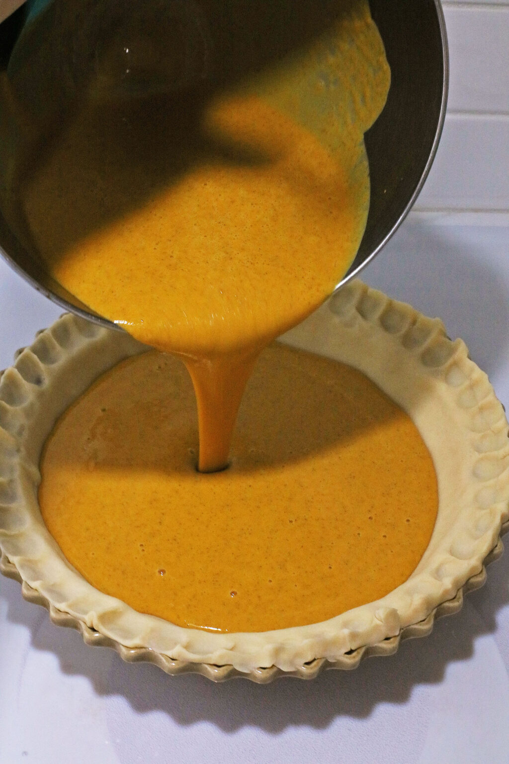 pumpkin pie mixture being poured into pie crust