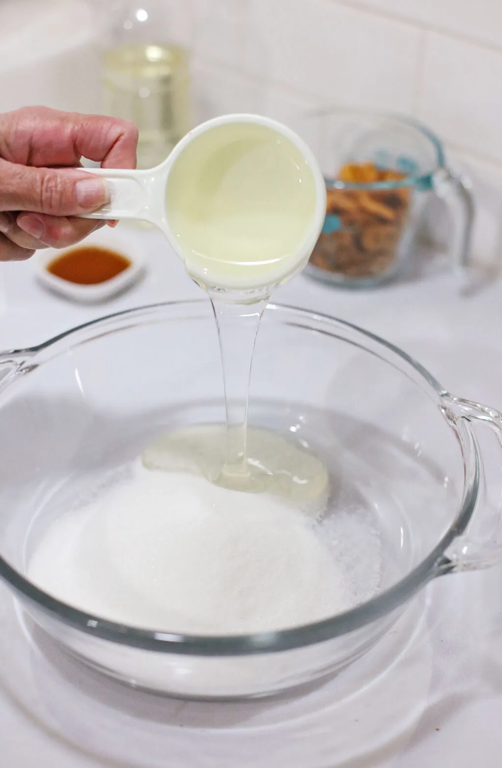 hand pouring corn syrup into large glass bowl with sugar