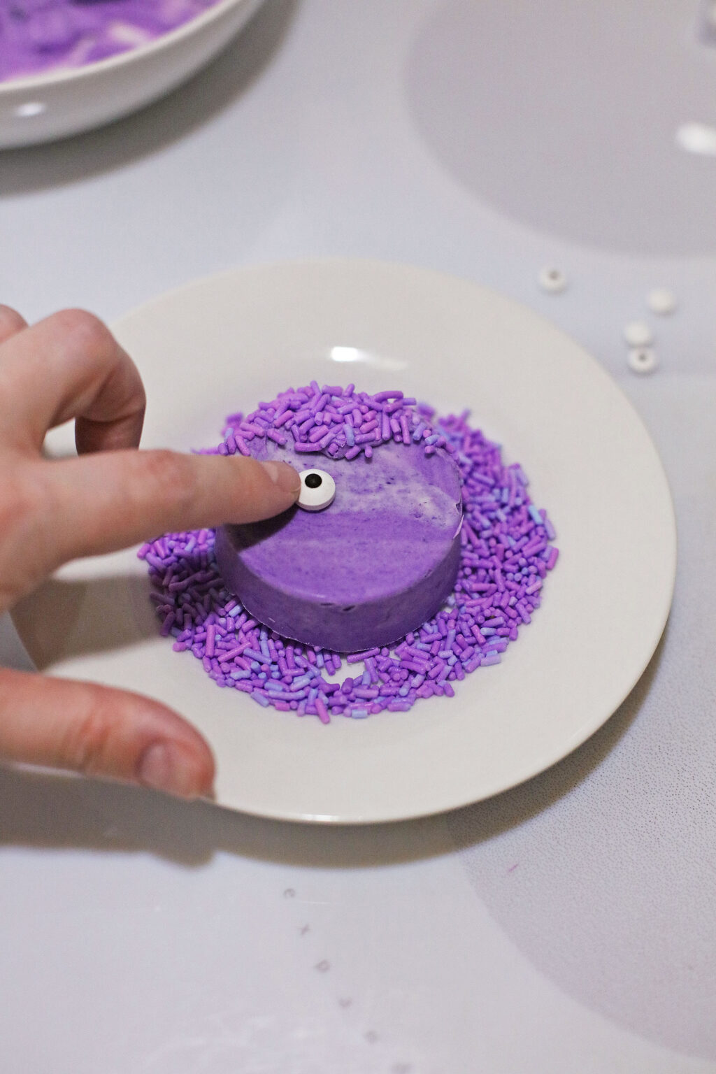 hand putting candy eyeballs onto purple oreo