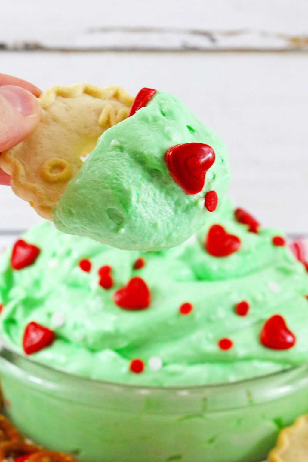 woman's hand dipping cookie into grinch dip