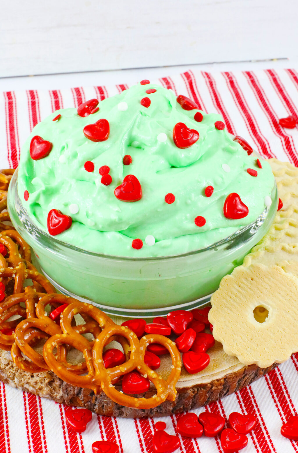large clear bowl of grinch dip on a table with pretzels