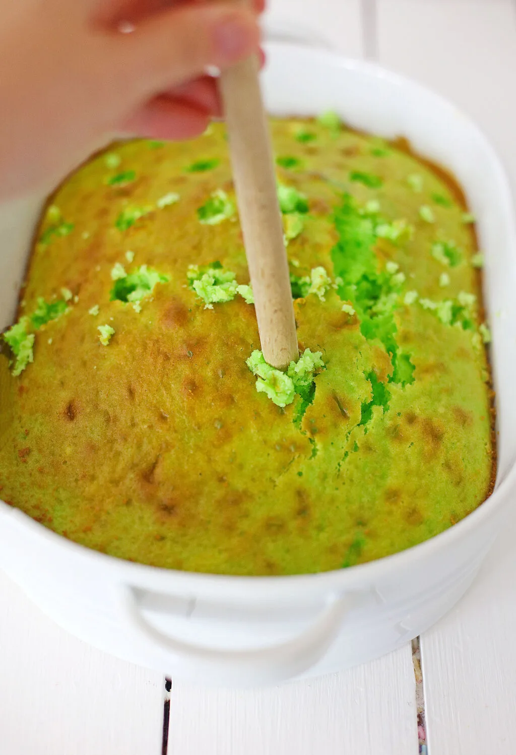 using wooden spoon to poke holes in green cake