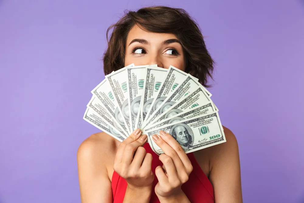 woman holding wad of cash of unclaimed money on purple background