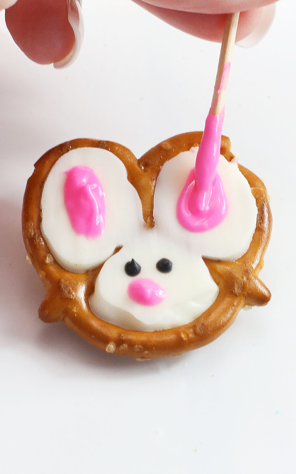 hand using toothpick to make pink ears on bunny pretzels