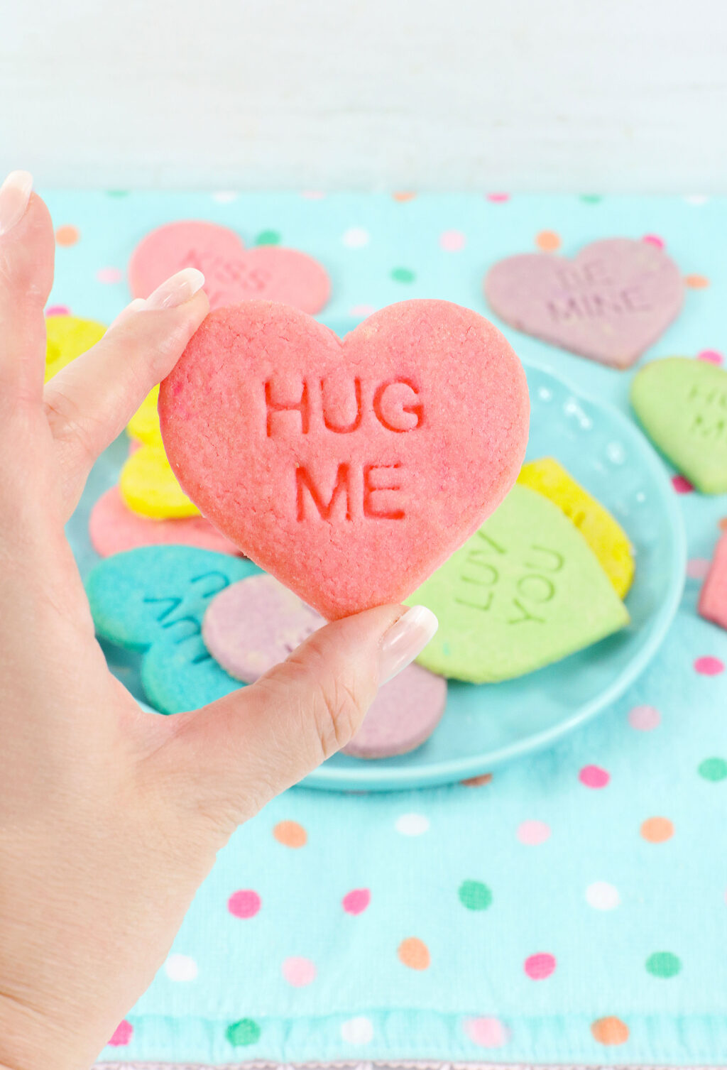 woman's hand holding a conversation heart cookie that says hug me