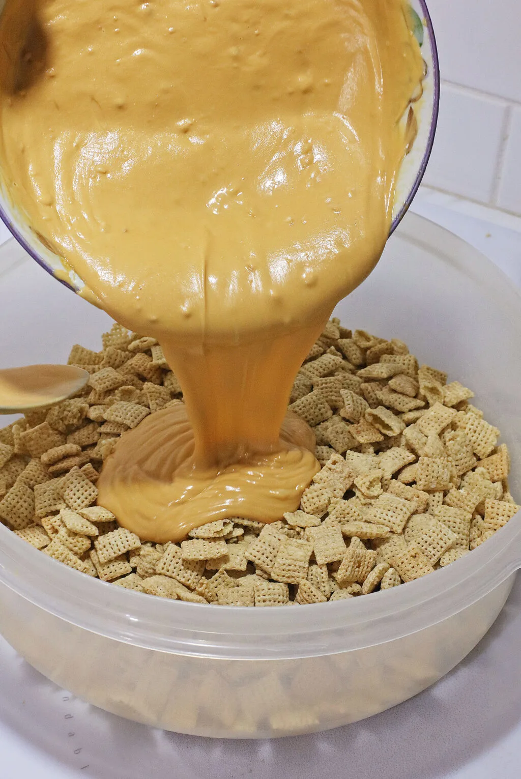 bowl of melted peanut butter being poured of chex mix cereal