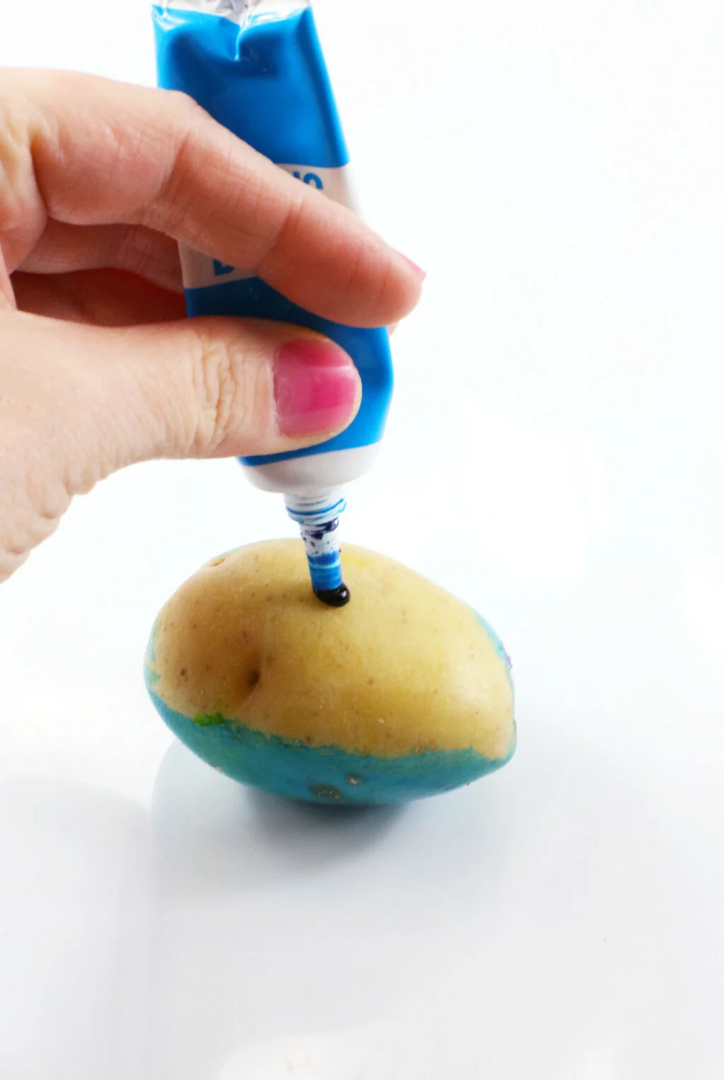 hand putting drop of blue food coloring on a potato