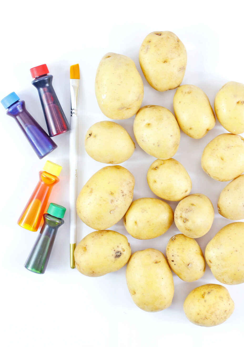 yellow potatoes with regular food coloring and a paintbrush next to it on a white table