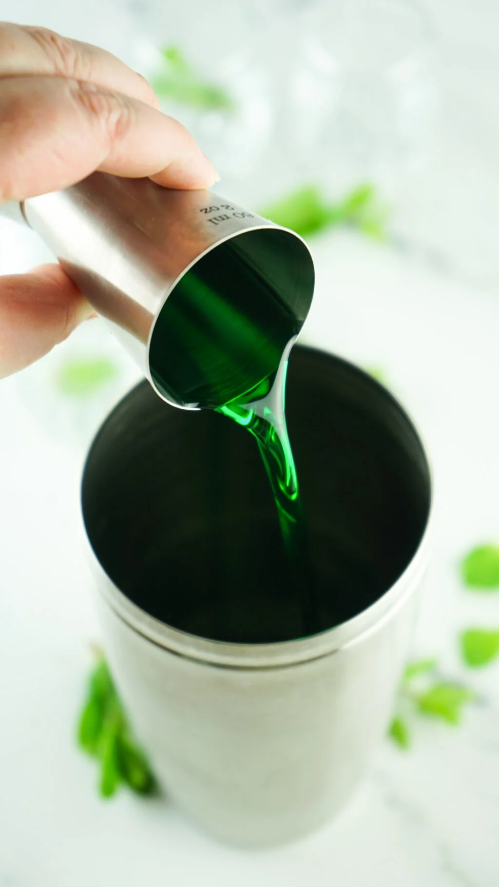green ingredient being poured into cocktail shaker
