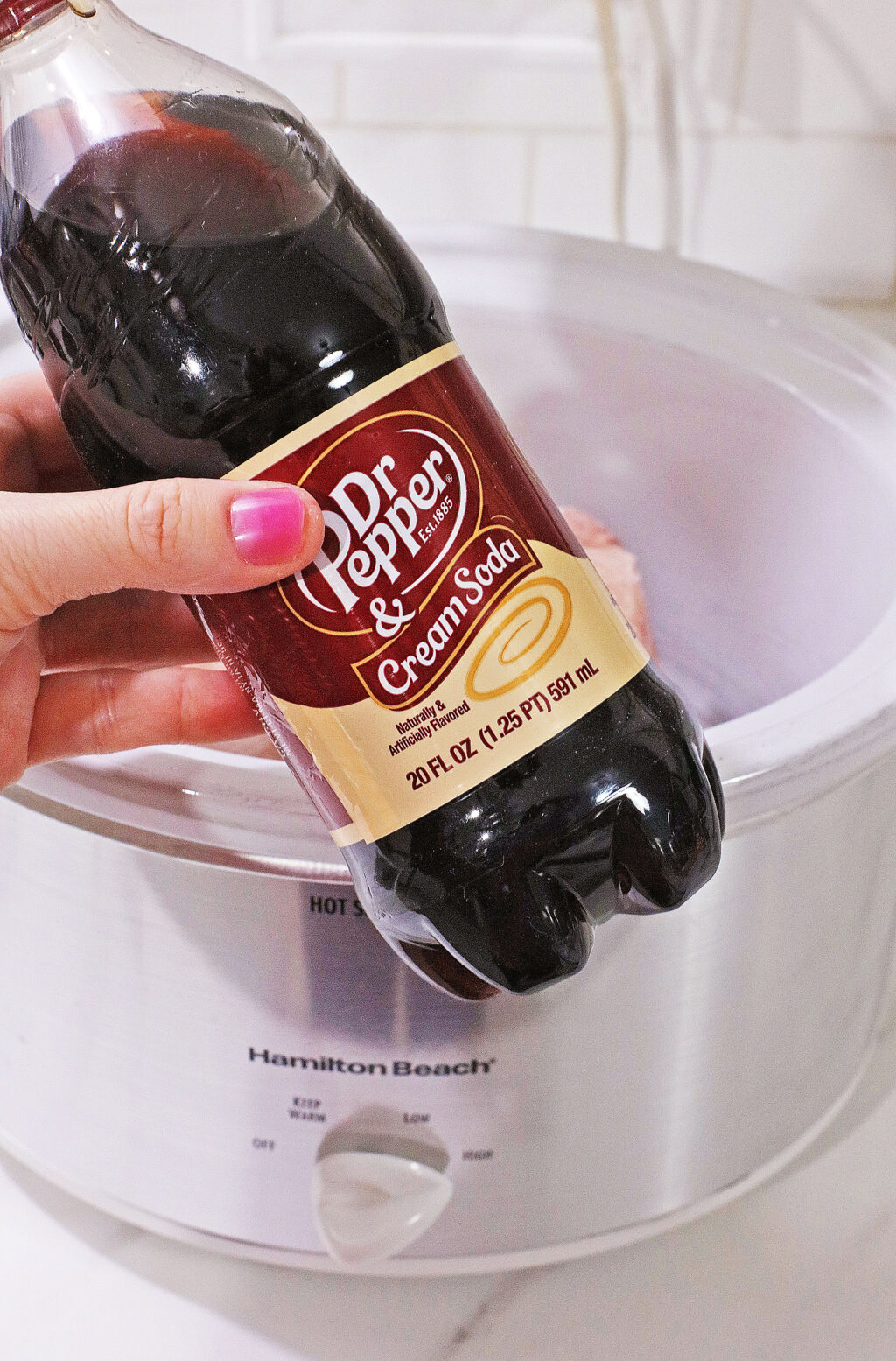 woman's hand pouring dr. pepper over top of pork roast