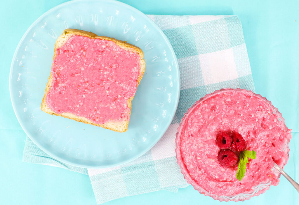 raspberry butter in a bowl next to a slice of bread with butter spread on top