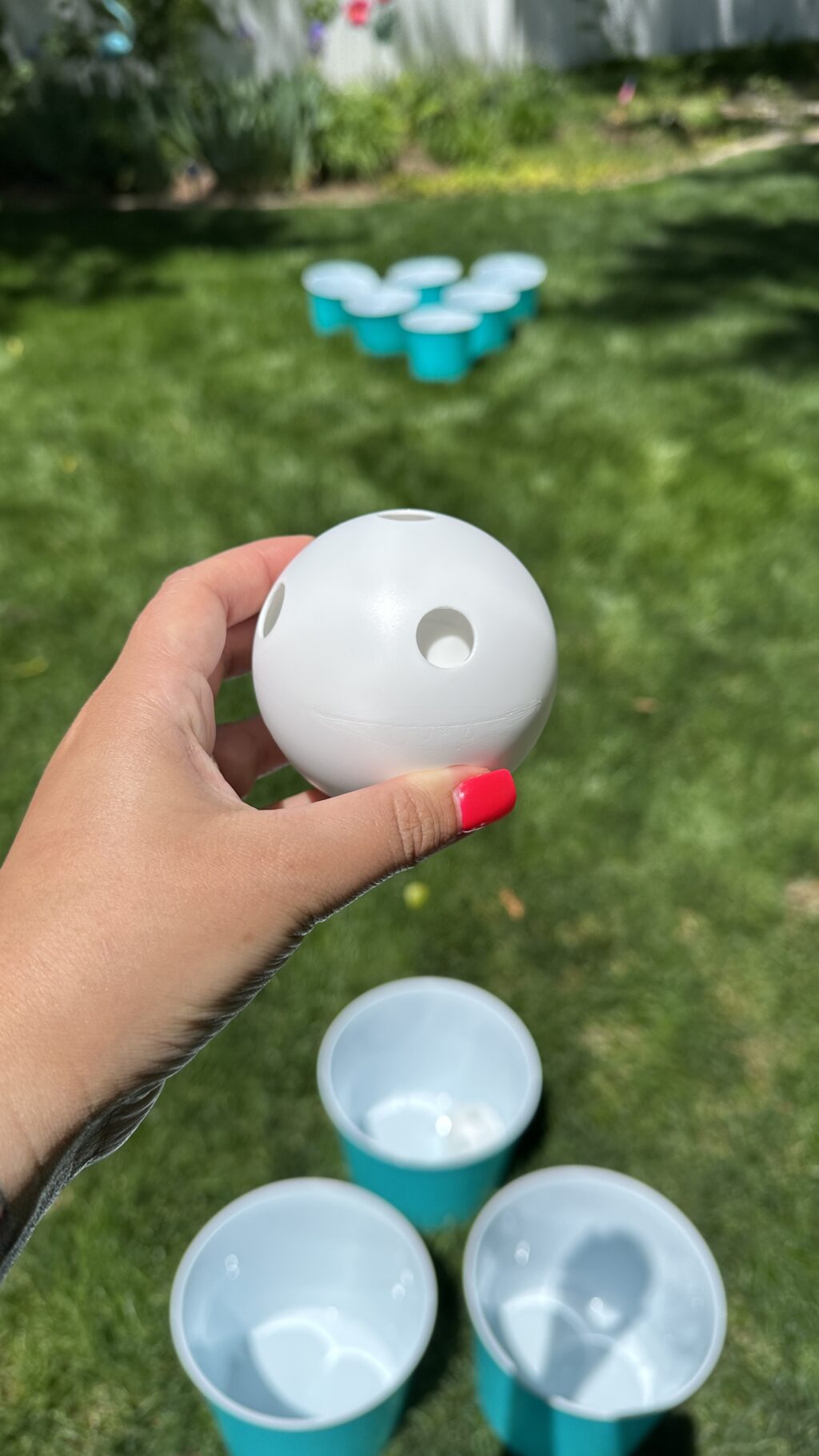 woman's hand holding plastic ball to play giant yard pong