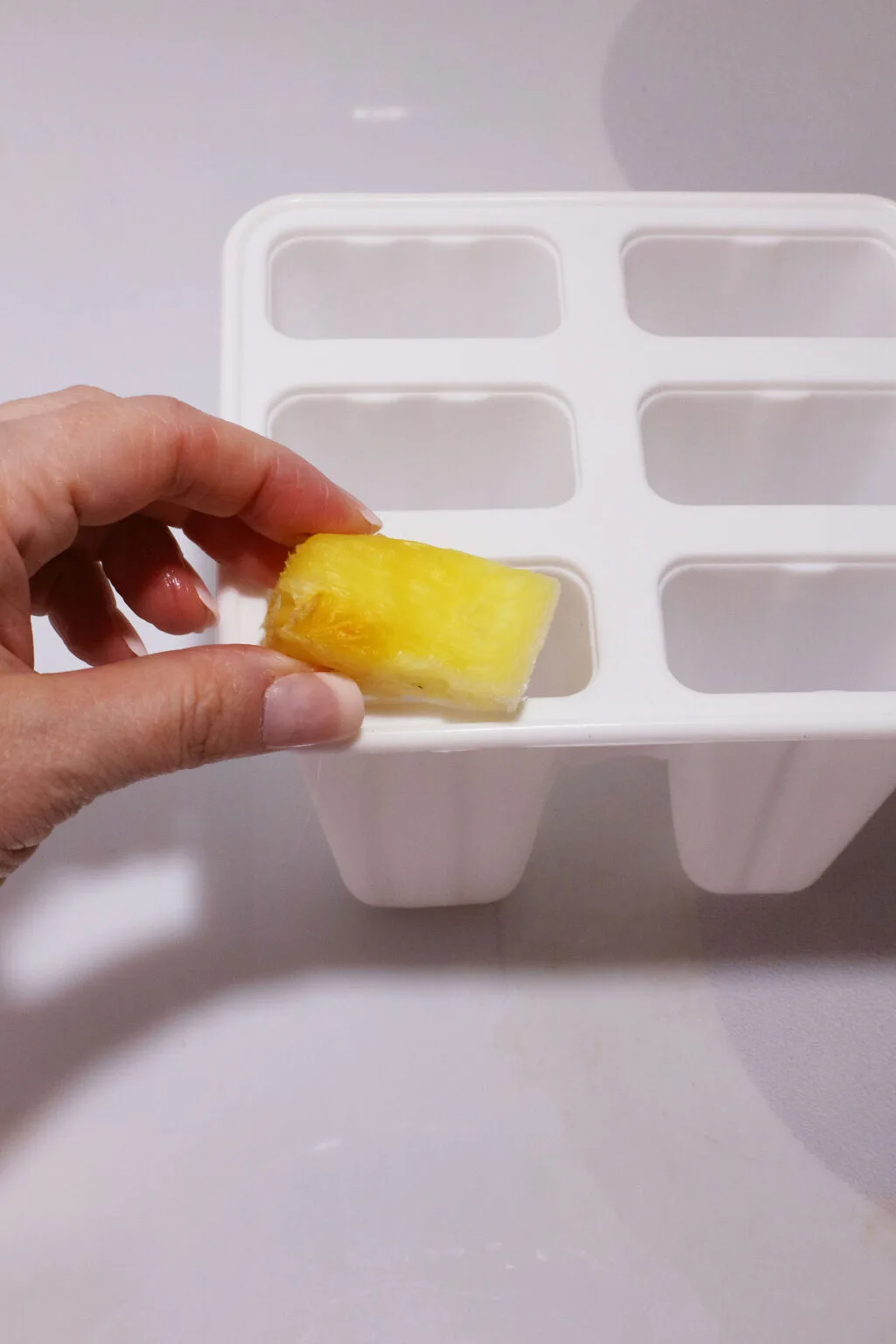 putting piece of pineapple into bottom of popsicle mold