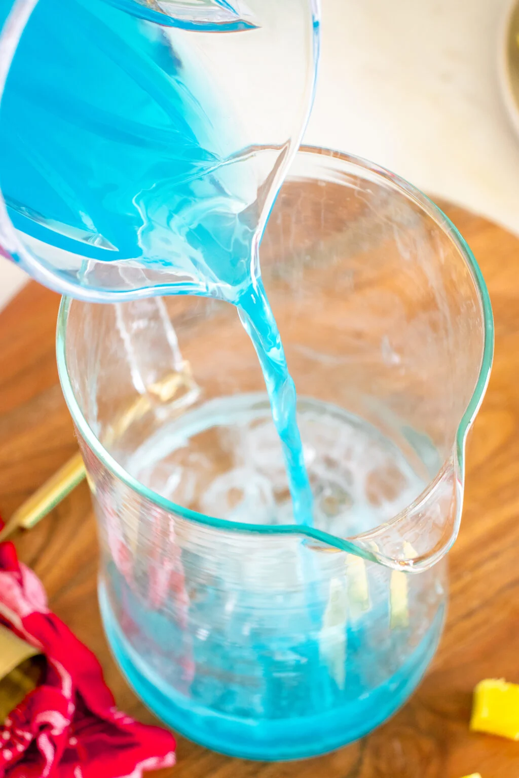 pouring blue hawaiian cocktail mixture into a large pitcher