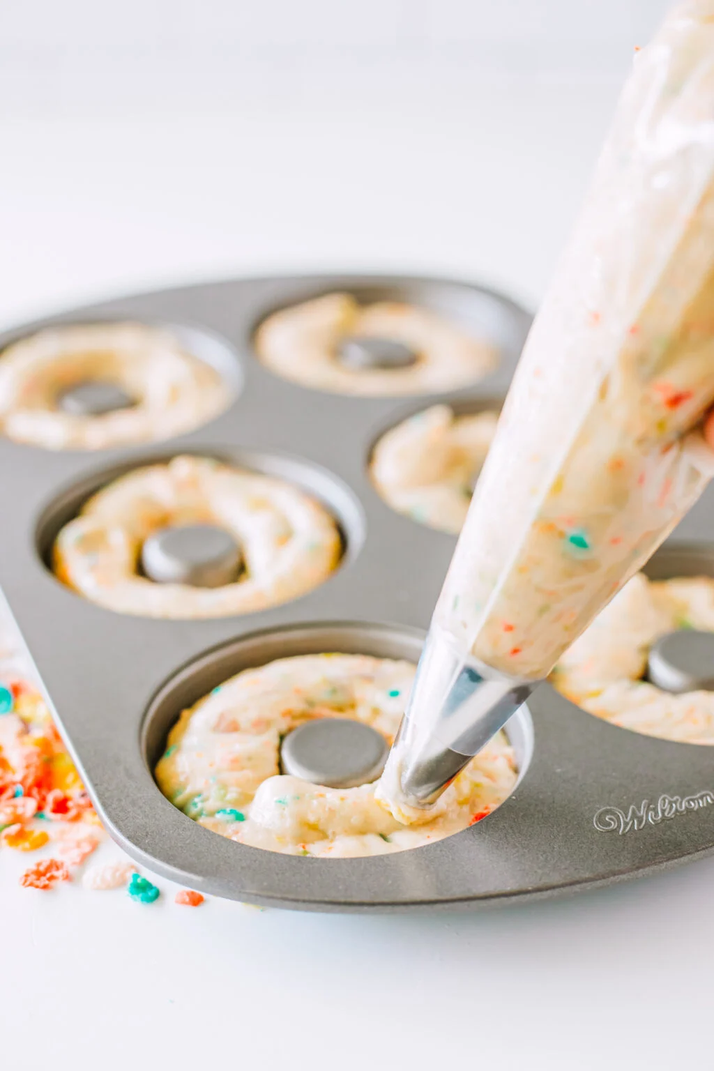 piping bag filling donut pan with fruity pebbles donut batter