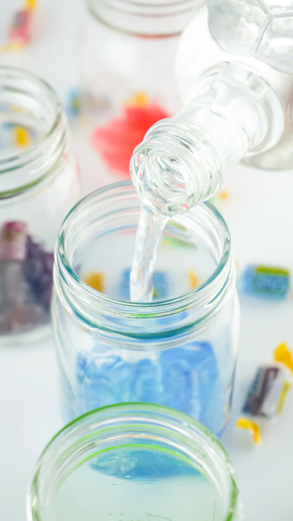 pouring vodka into mason jar filled with blue jolly ranchers
