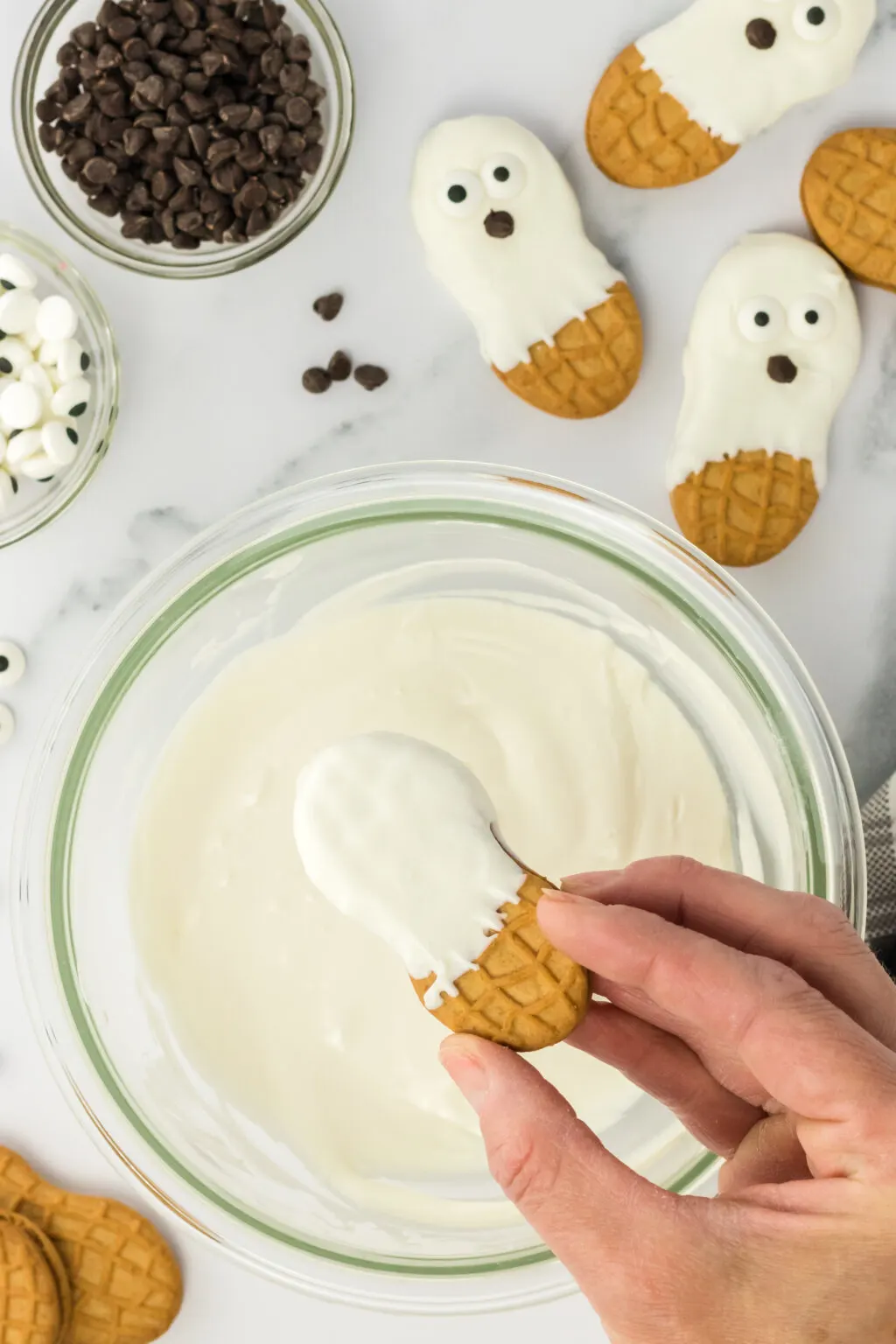 nutter butter cookie being dipped into melted white chocolate to make a ghost cookie