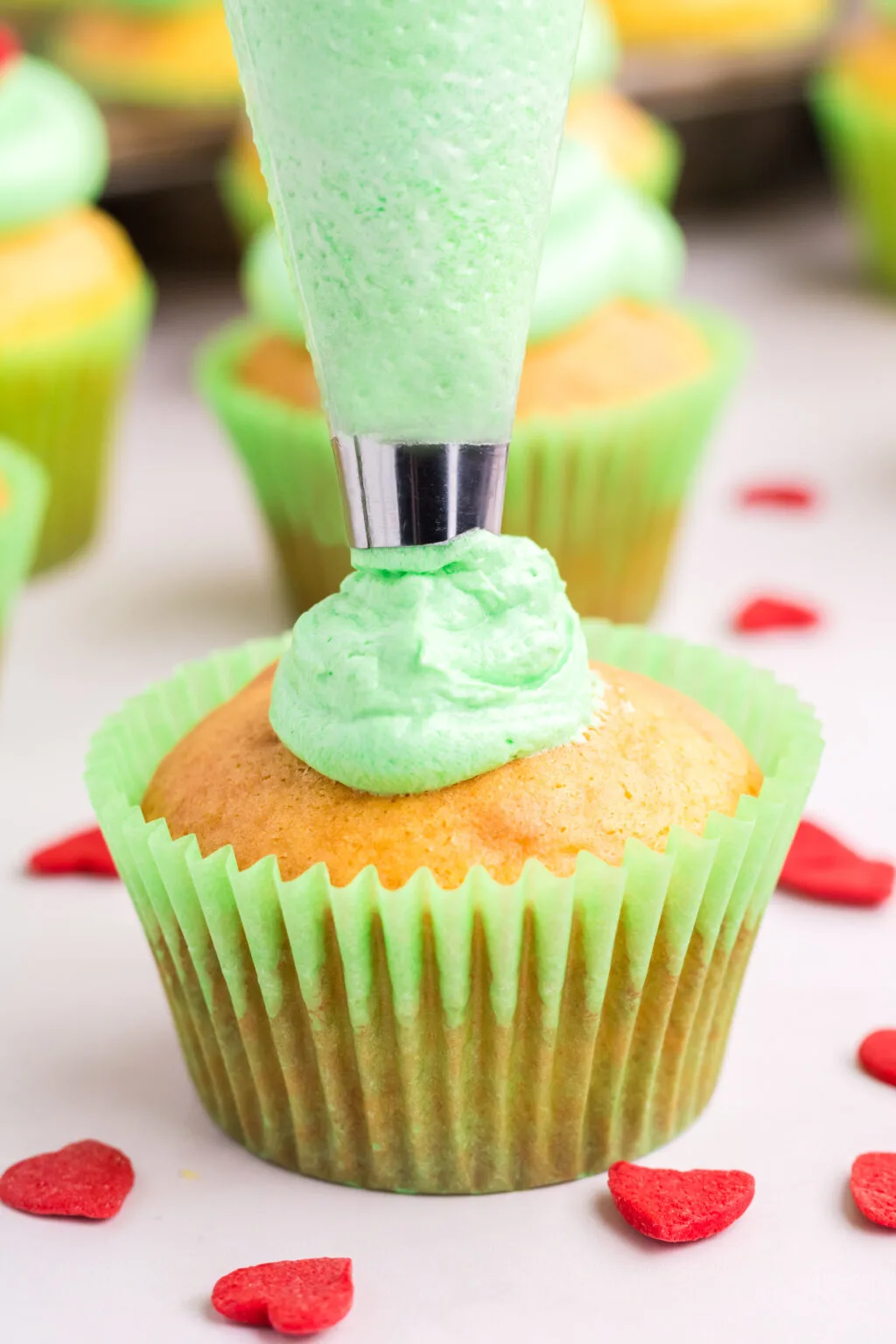 frosting the top of a grinch cupcake with green frosting