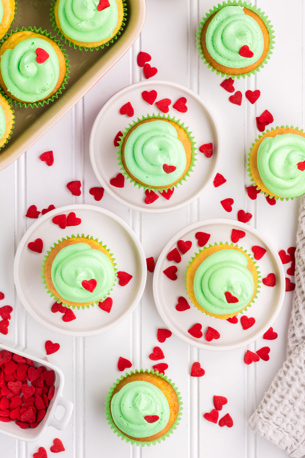 grinch cupcakes on table with white plates and heart sprinkles