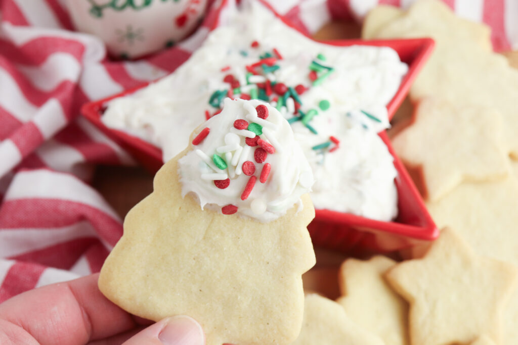 hand holding christmas cookie with christmas sugar cookie dip on it